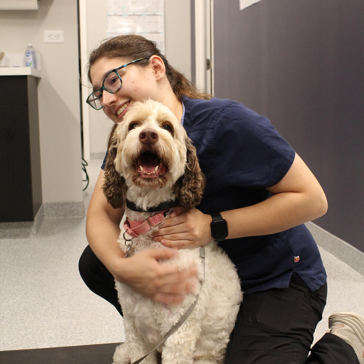 Woman And Happy Dog female vet staff member embraces happy dog on floor of exam room
